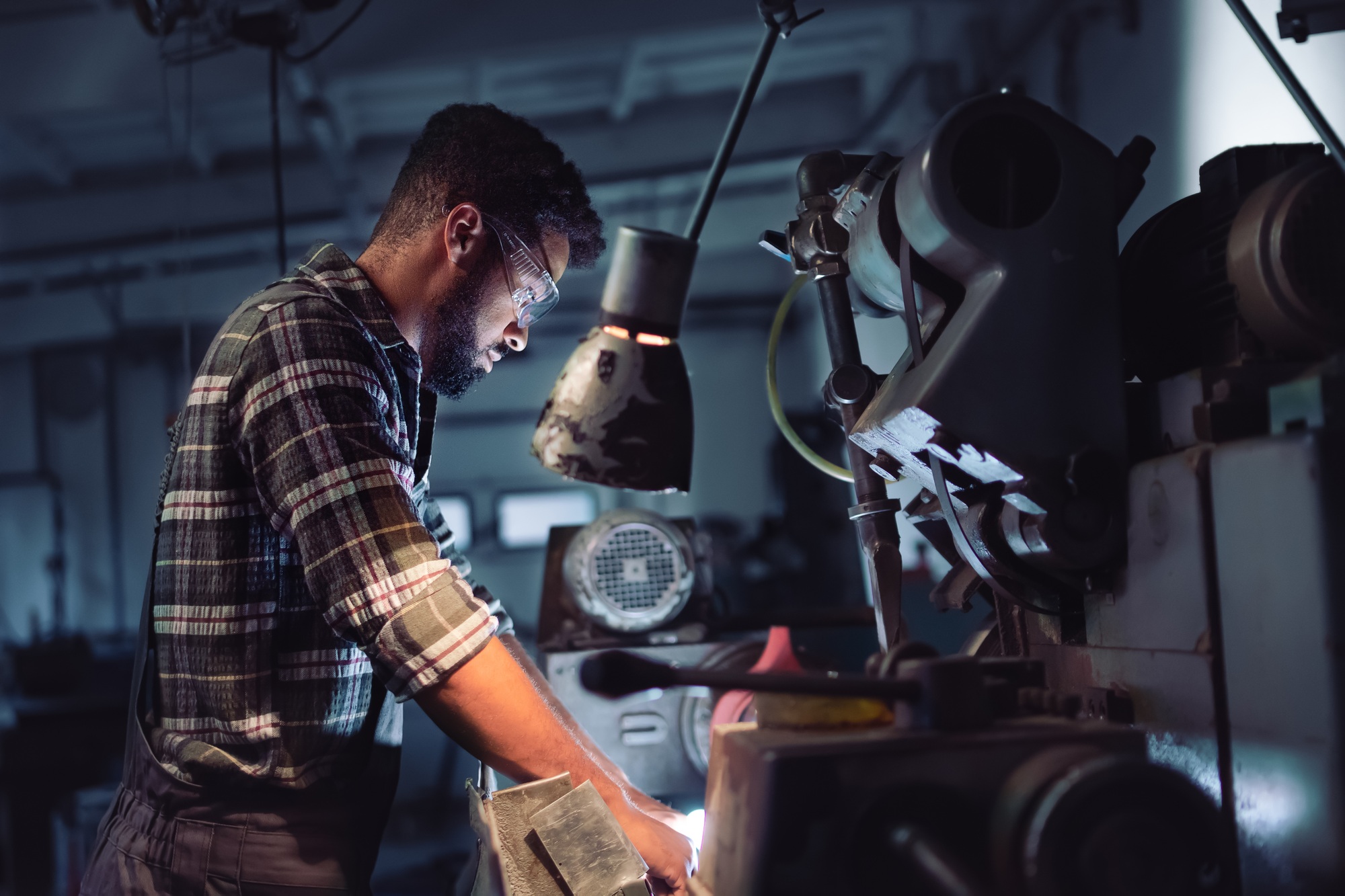 Portrait of young concentrated african american man working on cutter indoors in metal workshop